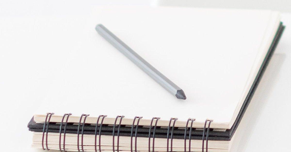 Beyaz masada spiral ciltli defter ve üzerinde duran kalem